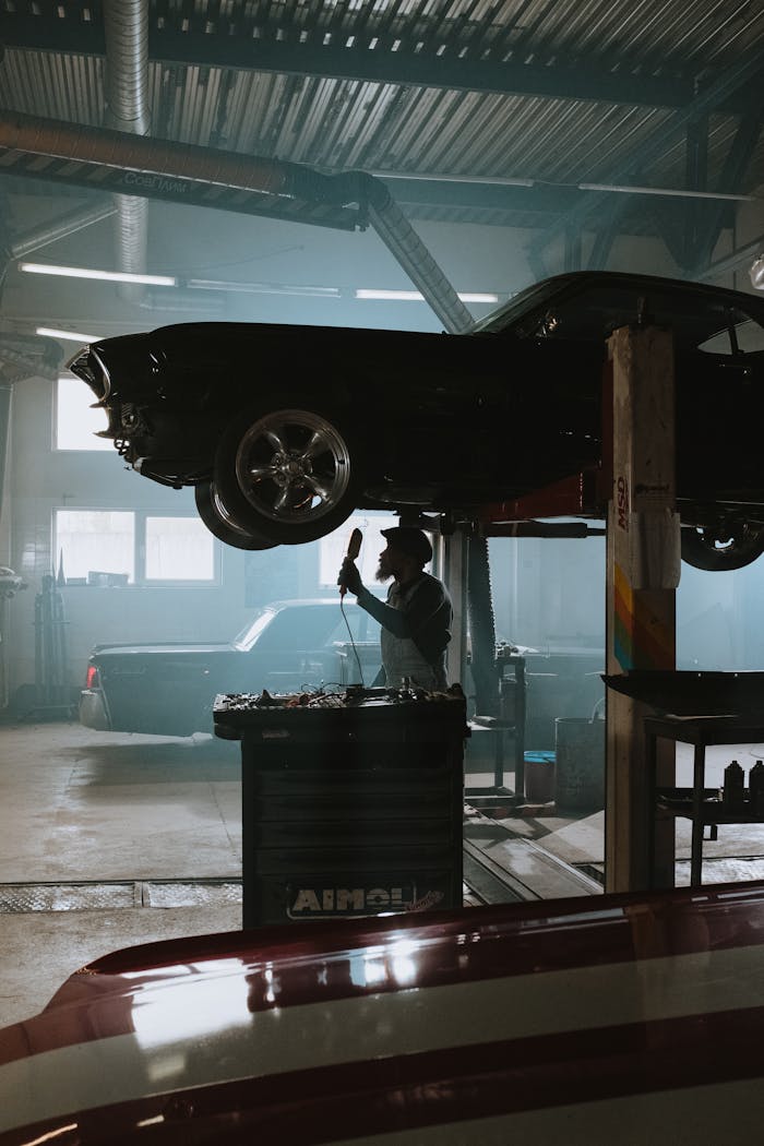 A mechanic inspects a car on a lift inside a bustling automotive garage.